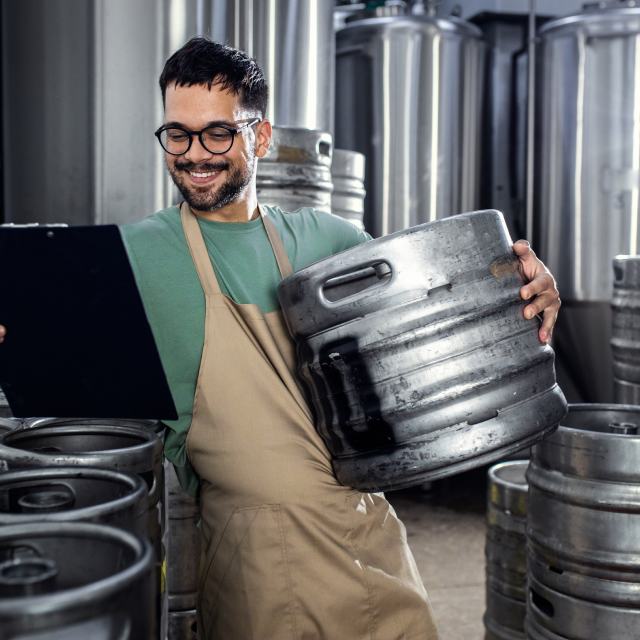 Man working in craft brewery carrying metal barrel